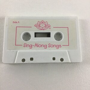 May include: White cassette tape with a pink flower logo and the text "Sing-Along Songs" on the front. The tape is labeled "Side A".