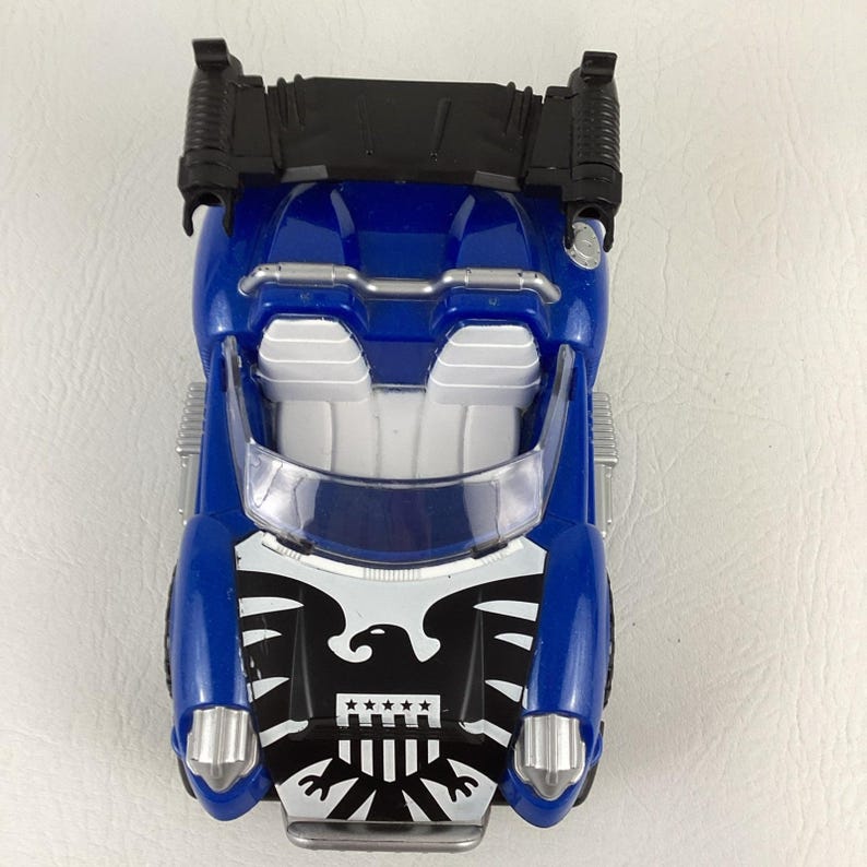 May include: A blue toy car with a black top and silver accents. The front features a black and white eagle emblem. The car has a clear windshield and white interior details. A fun toy for kids.
