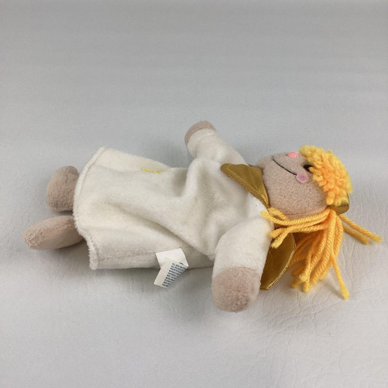 Puede incluir: Una mu&ntilde;eca de &aacute;ngel de peluche con una t&uacute;nica color crema, brazos y piernas color canela y una cara sonriente con mejillas rosadas. La mu&ntilde;eca tiene alas doradas y cabello de hilo amarillo. Una peque&ntilde;a etiqueta est&aacute; adherida a la t&uacute;nica.