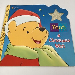 May include: A children's book titled "Pooh: A Christmas Wish" featuring a smiling Winnie the Pooh wearing a Santa hat and green scarf. The cover is blue with a glittery star and the Golden Books logo.