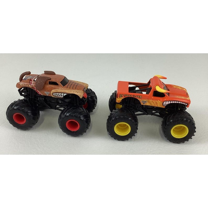 May include: Two toy monster trucks. One is brown with a dog-like design and the text "Monster Mutt". The other is orange with a bull design and the text "El Toro Loco". Both have large black tyres with red and yellow accents.