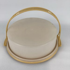 Peut inclure: Un récipient rond beige avec une poignée assortie. Le récipient a un couvercle et une base, et la poignée est arquée sur le dessus. Le récipient en plastique est probablement destiné au stockage ou au transport d'aliments.