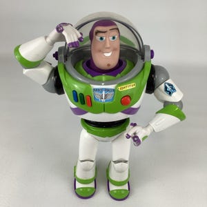 May include: A Buzz Lightyear action figure in a classic pose. The figure features a green, white, and purple spacesuit with the words "SPACE RANGER" and "LIGHTYEAR" printed on the chest. The figure has a clear helmet and is approximately 12 inches tall.
