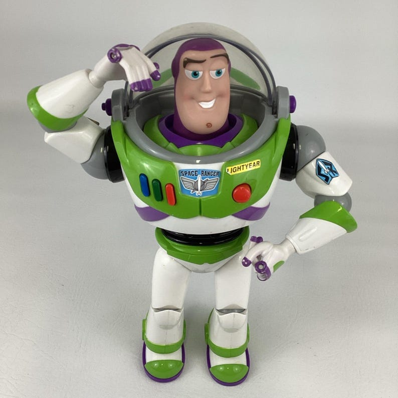 May include: A Buzz Lightyear action figure in a classic pose. The figure features a green, white, and purple spacesuit with the words "SPACE RANGER" and "LIGHTYEAR" printed on the chest. The figure has a clear helmet and is approximately 12 inches tall.