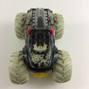 May include: A black monster truck toy with a camouflage pattern and red horns. The truck has large, white tires and a detailed engine.