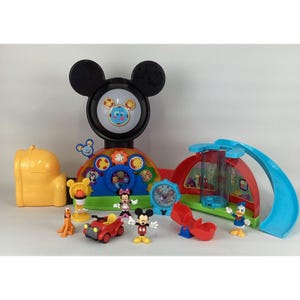 Pu&ograve; includere: Un colorato playset di Mickey Mouse Clubhouse con una grande testa di Topolino, un'auto rossa e varie statuette di personaggi. Il set include uno scivolo, un orologio e altri elementi interattivi, il tutto in colori primari vivaci.