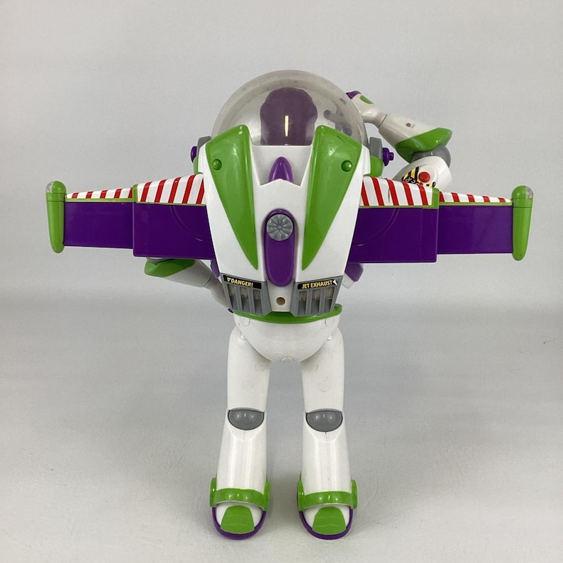 May include: A Buzz Lightyear action figure, featuring a white body, green and purple accents, and a clear helmet. The figure has red and white striped wings and the words "JET EXHAUST" and "DANGER" printed on the back.