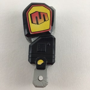 May include: Black and gray plastic toy with a yellow and red logo that says "SM" on it. The toy has a gray handle and a black body.