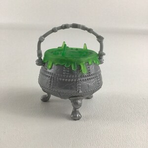 May include: A silver cauldron with a green slime lid and a handle. The cauldron has three legs and is decorated with a pattern of dots and lines.
