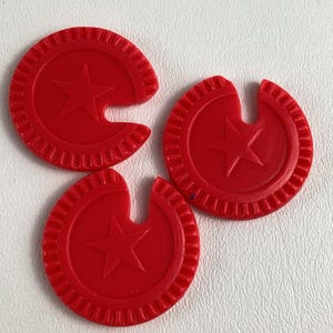 Op de afbeelding: Drie rode plastic spel fiches. Elke fiche is cirkelvormig met een ster in het midden en een gekerfde rand. De fiches hebben een heldere, effen rode kleur.