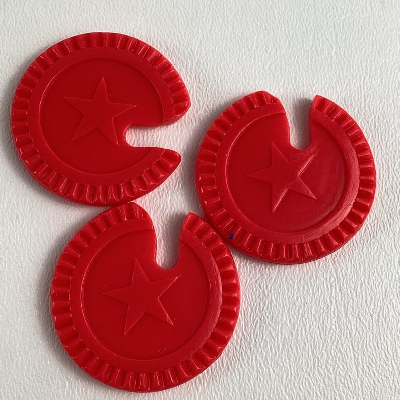 Op de afbeelding: Drie rode plastic spel fiches. Elke fiche is cirkelvormig met een ster in het midden en een gekerfde rand. De fiches hebben een heldere, effen rode kleur.