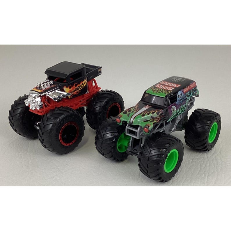 May include: Two toy monster trucks. One is red with black wheels and a silver engine. The other is green and black with a skull design and green wheels. Both have large, black tires.