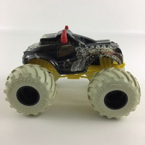 May include: Black monster truck toy with red horns, yellow wheels, and a white tire tread. The truck has a camouflage pattern and the words "Monster Trucks" on the side.