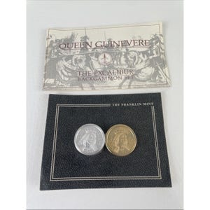 May include: A silver and gold coin set from The Franklin Mint, featuring Queen Guinevere. The coins are displayed on a black background with the text "THE FRANKLIN MINT". The set includes a card with the text "QUEEN GUINEVERE THE EXCALIBUR BACKGAMMON SET".