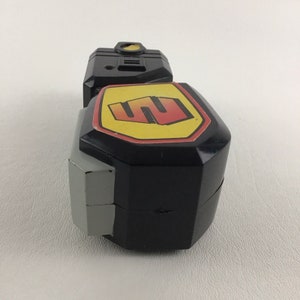 May include: Black and gray toy with a yellow and red logo that says "S".