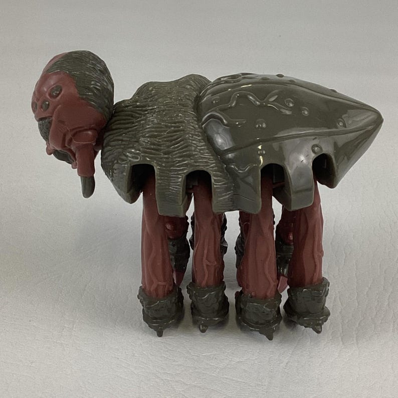 K&ouml;nnte beinhalten: Eine Kunststoff-Spielfigur in Form eines Wesens mit dunkelrotem Kopf und mehreren Augen, einem strukturierten grauen R&uuml;ckenpanzer sowie acht langen, dunkelroten Beinen mit grauen F&uuml;&szlig;en. Die Figur hat ein segmentiertes Aussehen mit gl&auml;nzendem Panzer.