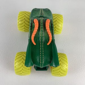 Pu&ograve; includere: Giocattolo di monster truck verde con pneumatici gialli. Il camion presenta tentacoli arancioni e una carrozzeria verde strutturata. I pneumatici sono di colore giallo brillante e il design ricorda una creatura.