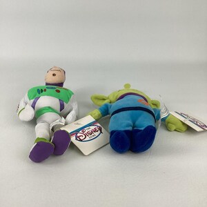 Pu&ograve; includere: Due peluche, un personaggio di Buzz Lightyear in tuta spaziale bianca, verde e viola e un alieno verde a tre occhi in tuta blu. Entrambi i giocattoli morbidi hanno etichette di carta bianca con il logo rosso e blu di The Disney Store.