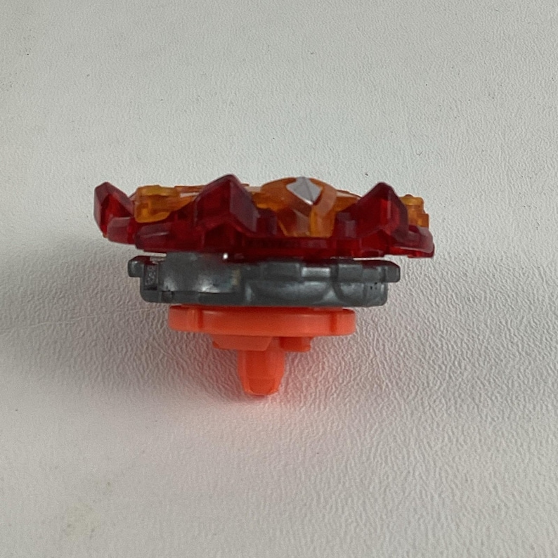 May include: A red, orange, and silver toy top with a multi-layered design. The top features a red, spiky outer layer, an orange center, and a silver base. The bottom has an orange, pointed tip.