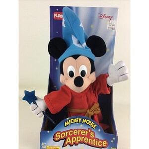 May include: A plush Mickey Mouse toy dressed as Sorcerer's Apprentice from the Disney movie Fantasia. He is wearing a blue hat, red robe, and holding a blue star wand. The packaging features the Disney logo and the words "Mickey Mouse Sorcerer's Apprentice".