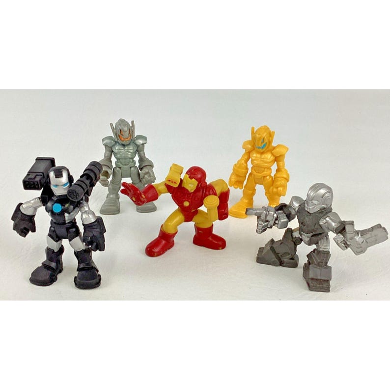 May include: A collection of five colorful action figures. The figures include a red and gold Iron Man, a silver and black War Machine, and three other robot-like characters in silver and yellow. The toys are posed on a white surface.