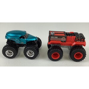 Pu&ograve; includere: Due monster truck giocattolo. Uno &egrave; turchese con ruote nere e cerchi argentati. L'altro &egrave; un camion dei pompieri rosso con dettagli neri e ruote rosse. Entrambi hanno grandi pneumatici fuoristrada.