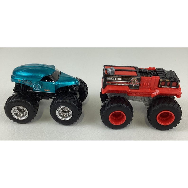 Pu&ograve; includere: Due monster truck giocattolo. Uno &egrave; turchese con ruote nere e cerchi argentati. L'altro &egrave; un camion dei pompieri rosso con dettagli neri e ruote rosse. Entrambi hanno grandi pneumatici fuoristrada.