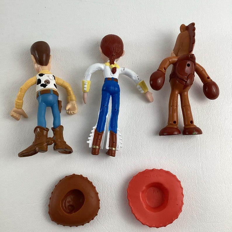 May include: A collection of Toy Story character figurines, including Woody, Jessie, and Bullseye, along with a brown cowboy hat and a red tire-shaped object. The figures are in various poses, showcasing their distinct outfits and features.
