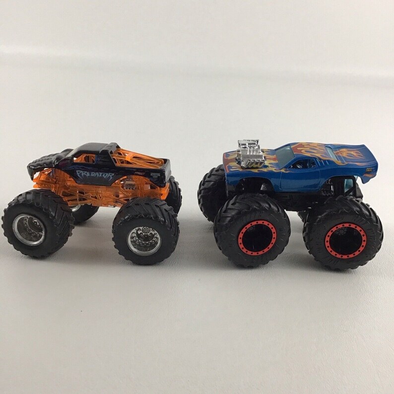 May include: Two toy monster trucks, one orange and black with "PREDATOR" on the side, and one blue with flames on the side.