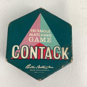 May include: A hexagonal game box for the Contack triangle matching game by Parker Brothers Inc. The box is dark teal with a large central triangle graphic in pink and light blue. The text reads TRIANGLE MATCHING GAME CONTACK.