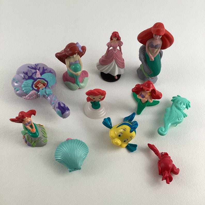 May include: A collection of small, colorful figurines featuring characters from a popular animated film. The figurines include a mermaid, a fish, a seahorse, and other sea-themed characters. The figurines are made of plastic and are various sizes.