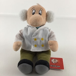 May include: A plush toy of Professor Ochanomizu, the creator of Astro Boy, from the Astro Boy anime series. The plush toy is wearing a white lab coat with yellow buttons and green pants. The toy has a tag that says "Astro Boy" on it.