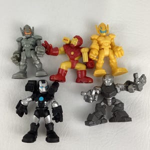 May include: A collection of five toy action figures in various colors. The figures include Iron Man, Ultron, and other characters. The toys are made of plastic and have detailed designs. The figures are posed in dynamic positions.