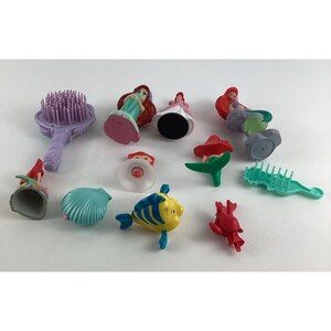 May include: A collection of colorful miniature figurines and accessories, including Ariel, Flounder, and other characters from The Little Mermaid. The set includes a purple brush, a seashell, and other themed items.