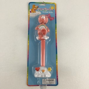 May include: A pink Care Bears Wobble Writer pen with a Care Bear character on top. The pen is packaged on a blue and white card with the Care Bears logo and the words "Wobble Writer" and "Colorful".