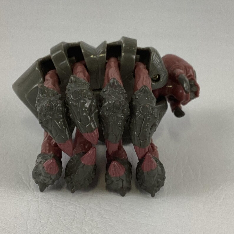K&ouml;nnte beinhalten: Eine Kunststoff-Actionfigur eines mehrbeinigen Wesens mit einem dunkelgrauen, segmentierten Panzer und rotbraunen Gliedma&szlig;en. Die Figur besitzt vier markante Beine mit texturierter grauer Panzerung und spitzen Enden sowie einen kleinen Kopf.