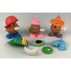 May include: Three brown potato-shaped figures with interchangeable plastic accessories including a red hard hat, blue shoes, pink bunny ears, an orange witch hat, purple shoes, a green hat, a blue base, a yellow and blue eye piece, and white teeth.