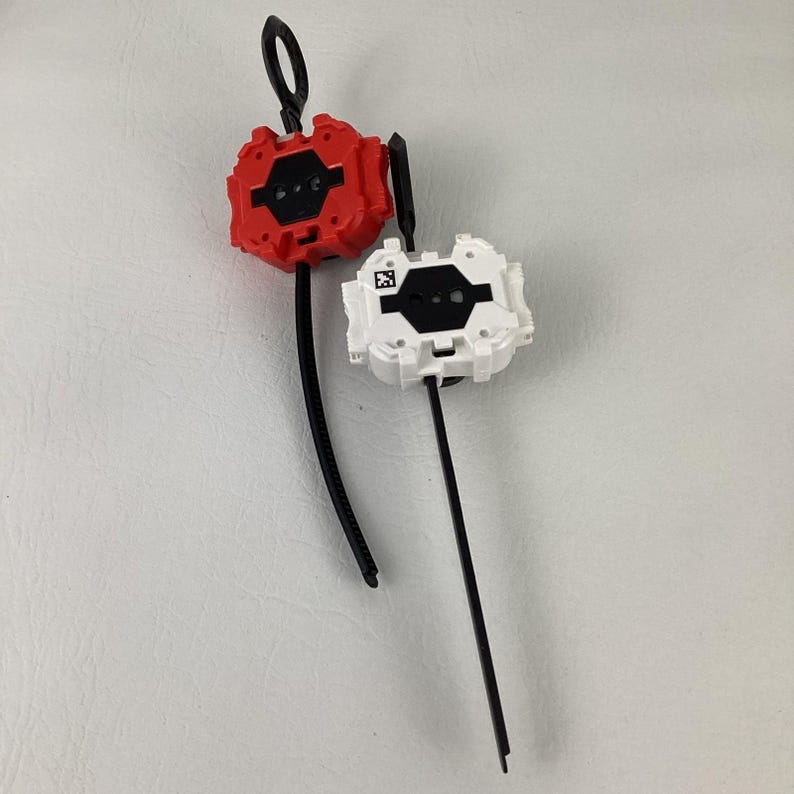 May include: Two plastic toy launchers, one red and one white, with black pull cords and loop handles. The launchers have a geometric design with black accents and a QR code.
