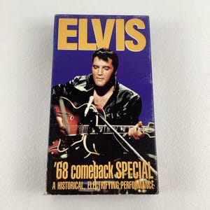 May include: A VHS tape featuring Elvis Presley playing a guitar. The tape cover is blue with yellow text that reads "Elvis '68 Comeback Special A Historical, Electrifying Performance."
