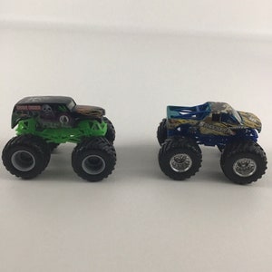 May include: Two monster truck toys, one black and green with "Grave Digger" written on the side, and the other blue, yellow, and green with "Shocker" written on the side.