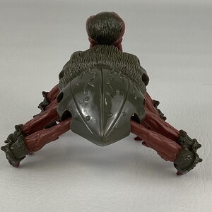 K&ouml;nnte beinhalten: Eine Kunststoff-Actionfigur eines mehrbeinigen Wesens mit einem dunkelolivgr&uuml;nen Panzer und strukturiertem R&uuml;cken. Die Figur hat rotbraune Gliedma&szlig;en mit dunkelolivgr&uuml;nen gepanzerten Manschetten an den Enden und ein abgerundetes, strukturiertes Kopfteil.