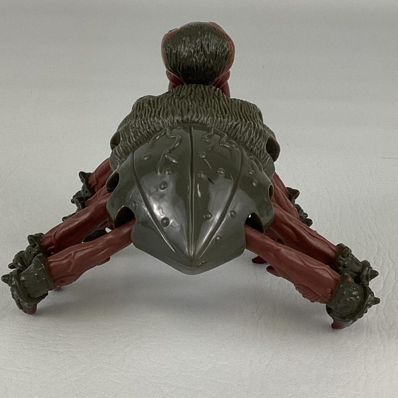 K&ouml;nnte beinhalten: Eine Kunststoff-Actionfigur eines mehrbeinigen Wesens mit einem dunkelolivgr&uuml;nen Panzer und strukturiertem R&uuml;cken. Die Figur hat rotbraune Gliedma&szlig;en mit dunkelolivgr&uuml;nen gepanzerten Manschetten an den Enden und ein abgerundetes, strukturiertes Kopfteil.