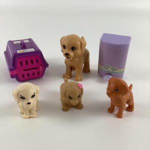 May include: A set of five plastic toy dog figurines, including a purple dog carrier, a purple dog food container, and three golden retriever puppies. One puppy is wearing a pink flower.