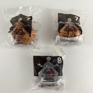 Könnte beinhalten: Drei Plastiktüten mit McDonald's Happy Meal Spielzeug. Die Spielzeuge sind Rückziehautomaten mit den Figuren aus dem Film 'Barney's Great Adventure'. Die Spielzeuge sind mit 7 und 8 nummeriert. Die Tüten sind aus durchsichtigem Plastik mit schwarzem und rotem Text.