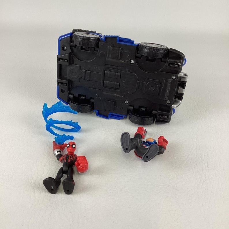 May include: A blue and black toy car with large black wheels is shown upside down. Two Spider-Man action figures are next to the car. One figure is standing and the other is lying down. A blue web-like accessory is also included.