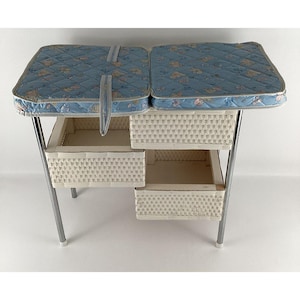 May include: A vintage baby changing table with a blue floral patterned cushion top. The table has three white wicker storage baskets and a silver metal frame. The changing table measures approximately 30 inches long, 20 inches wide, and 36 inches tall.