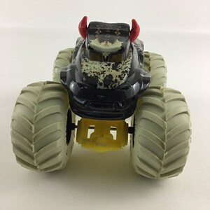 May include: Black monster truck toy with red horns and large gray tires. The truck has a camouflage pattern and yellow details.