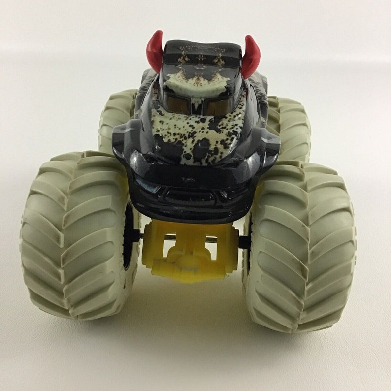 May include: Black monster truck toy with red horns and large gray tires. The truck has a camouflage pattern and yellow details.