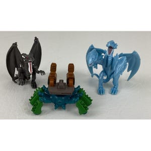 May include: Three toy figures: a black dragon with spread wings, a blue and green crab-like creature, and a light blue dragon with open mouth and wings. The figures are plastic and appear to be from a collectible series.