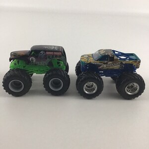 May include: Two monster truck toys, one green and black with "Grave Digger" written on the side, and the other blue and green with "Shockwave" written on the side.